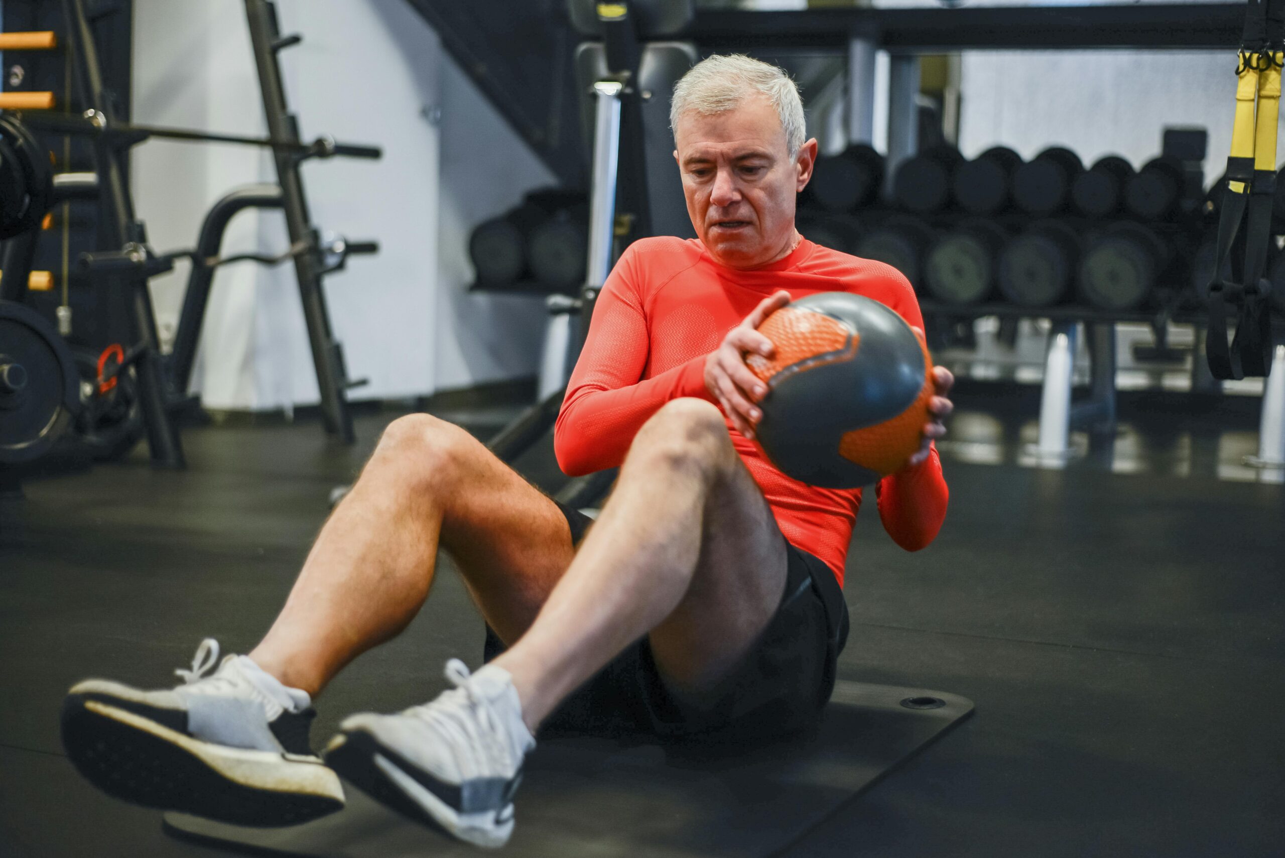 Elderly man in activewear performing medicine ball exercise at gym. Promotes healthy lifestyle.